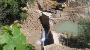 نمایی از عملیات اجرایی احداث سد در روستای گُلی بجنورد با حضور بیل مکانیکی و کارگران در کنار حوضچه آب و دیواره بتنی سد